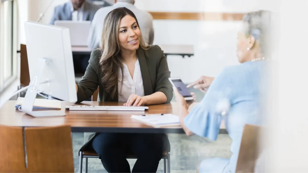 Consulente bancaria sorridente assiste una cliente che indica il suo smartphone