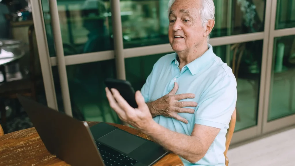 Un uomo anziano seduto usa laptop e smartphone per monitorare la sua respirazione