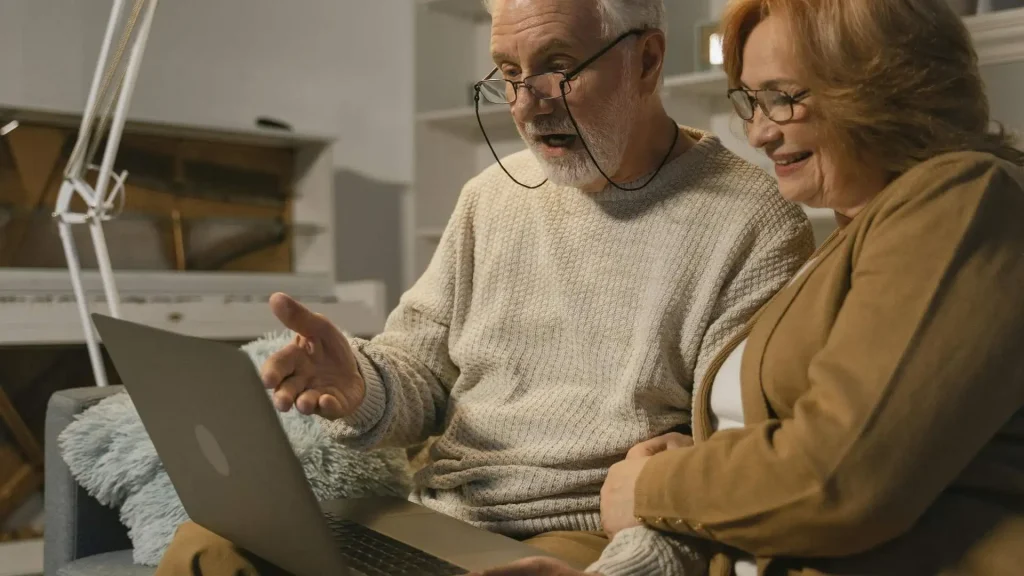 Coppia anziana seduta su un divano discute guardando lo schermo di un laptop