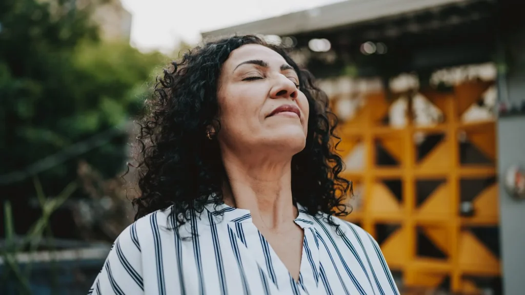 Una donna con gli occhi chiusi respira profondamente all’aperto